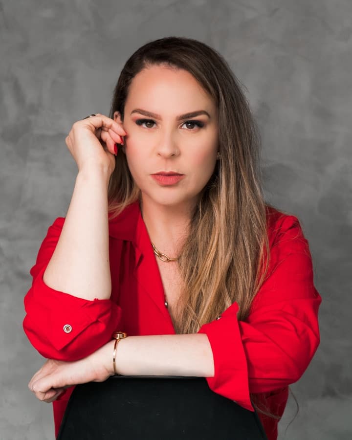 Carla Dias, a Carla da Hello, de camisa vermelha, apoiada em uma cadeira